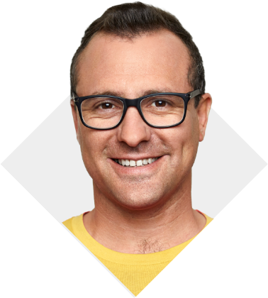 A man wearing prescription glasses and a yellow shirt smiling