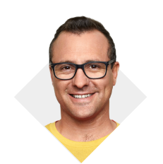 A man wearing prescription glasses and a yellow shirt smiling